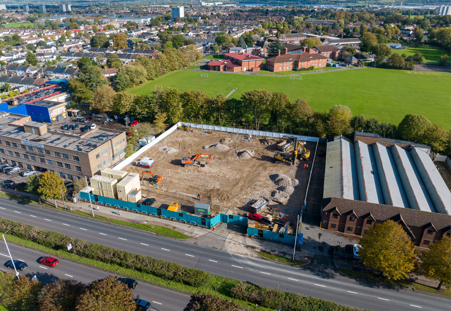 Aerial view of a construction site in a city. Excavator and bulldozer machines are visible along with piles of dirt.